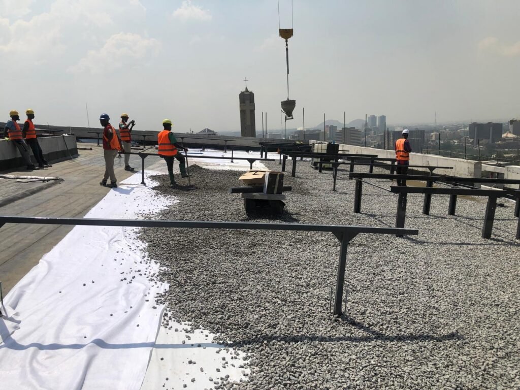 McMyra crew setting out the mounting rails on a ballasted flat roof, Abuja skyline behind
